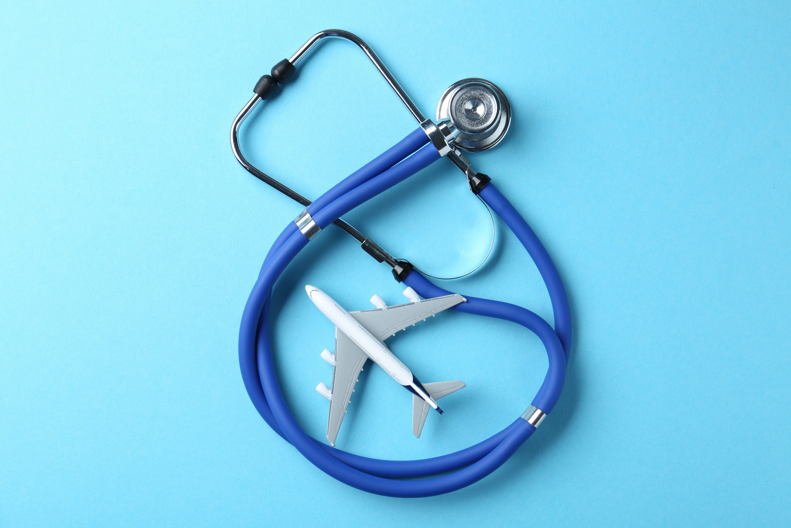 Medical tourism. Stethoscope and plane model on light blue background, top view